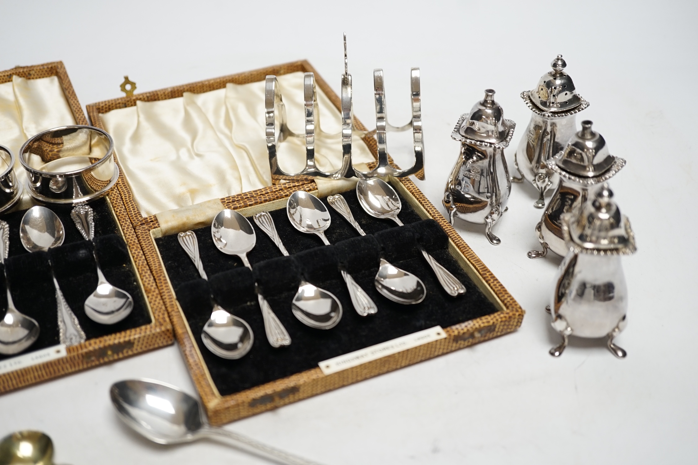 Two cased sets of six silver coffee spoons, a set of four silver condiments, two silver napkin rings, silver toastrack, etc.